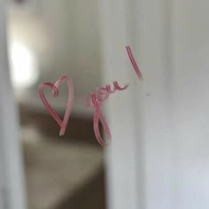 the word i love you written in pink ink on a glass door with a bed in the background