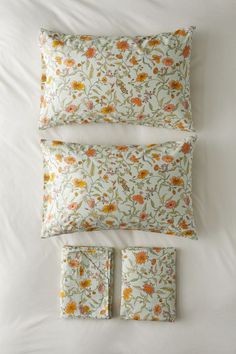 three pillows and two pillow cases on top of a white bed with floral print in the middle