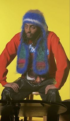 a man sitting on top of a wooden table wearing a blue and green fur hat