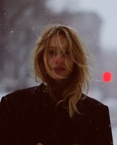 a woman standing in the snow with her hair blowing back and looking off into the distance