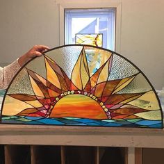 a woman is holding up a stained glass sunburst in front of a window