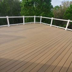 a wooden deck with white railings and trees in the background