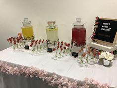 a table topped with lots of glasses filled with liquid and flowers next to a chalkboard