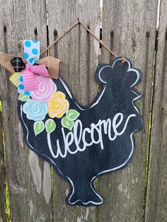 a welcome sign hanging on the side of a wooden fence with flowers and a bow