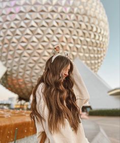 a woman with long hair wearing a tiara in front of the spaceship at disney world