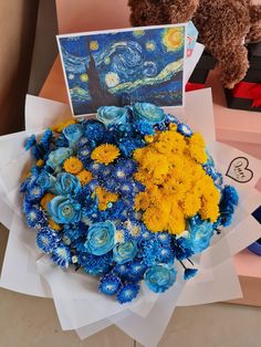 a bouquet of blue and yellow flowers next to a card with a painting on it