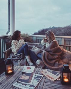 two women sitting on a deck talking to each other with candles in front of them