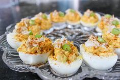 several deviled eggs are arranged on a glass platter with green onions and seasoning