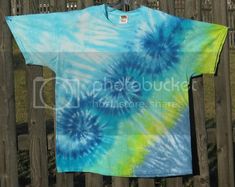 a blue and green tie - dyed t - shirt hanging on a wooden fence post