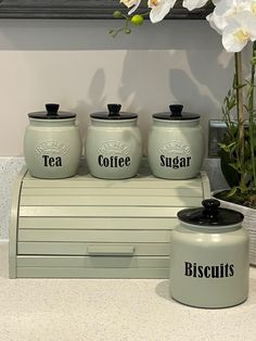 four green canisters sitting on top of a counter next to a vase with flowers