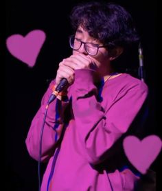 a man with glasses holding a microphone in front of heart shaped paper cutouts