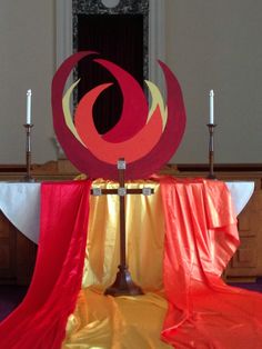 a red and yellow cloth draped around a metal stand with candles on the table in front of it