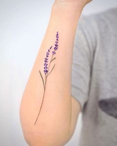 a woman's arm with a small purple flower tattoo on the left side of her arm