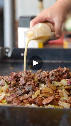 a person pouring sauce on food in a frying pan filled with meat and vegetables