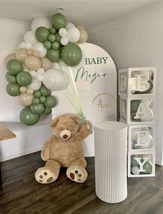 a teddy bear sitting on the floor in front of some balloons and a baby sign