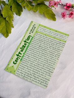 an open book sitting on top of a table next to pink flowers and green leaves