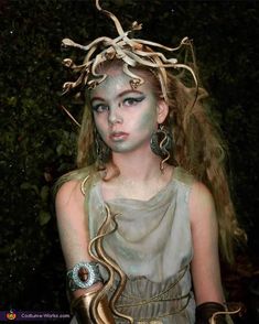 a woman with white makeup and gold accessories on her head, wearing snakes around her neck