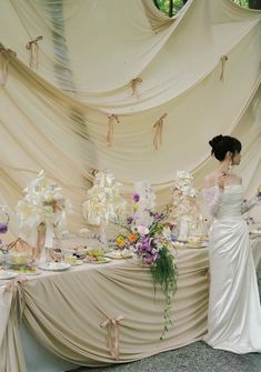 a woman in a white dress standing next to a table with flowers and cake on it