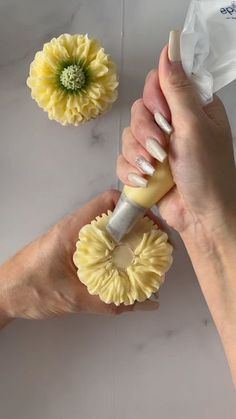 two hands holding yellow flowers and cleaning them with a sponge on a white table top