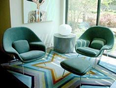 two green chairs sitting in front of a large window next to an ottoman and chair