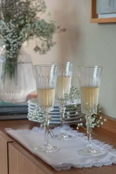 three champagne flutes are sitting on a table with white lace and baby's breath