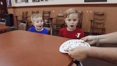 two children sitting at a table and one is holding a plate with food on it