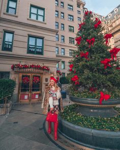 a woman standing next to a christmas tree in front of a tall building with red decorations