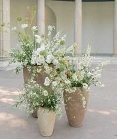 three vases filled with white flowers sitting on top of a cement floor next to each other