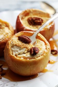 two baked apples with pecans and caramel sauce on a white plate, one has a spoon in it