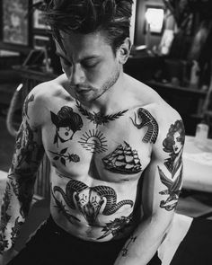 a man with many tattoos on his chest and arms is looking down at something in front of him