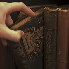 a person holding an open book in front of two books on a shelf next to each other