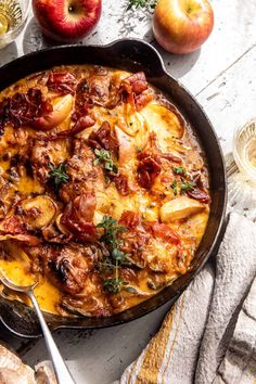 a skillet filled with meat and potatoes on top of a table next to apples