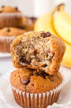 two chocolate chip muffins stacked on top of each other with bananas in the background