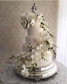 a wedding cake with white flowers on the top and initials on the bottom, sitting on a marble table