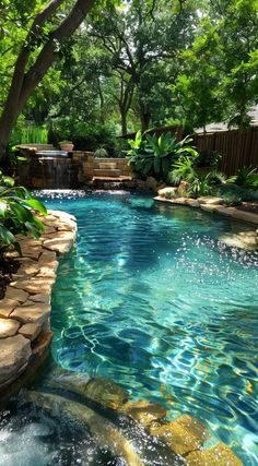 an outdoor swimming pool surrounded by lush green trees and rocks, with water flowing down the side