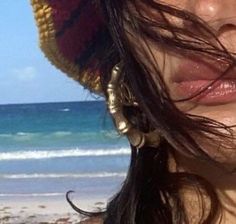 a close up of a person wearing a hat on the beach with water in the background