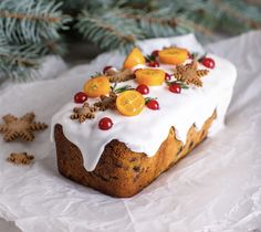 a cake with frosting and fruit on top sitting next to a pine tree branch