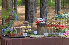 a table topped with lots of desserts next to trees