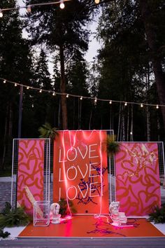 an orange and pink backdrop with love is in the air on it, surrounded by string lights