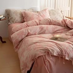 a bed with pink comforter and pillows in a room next to a lamp on a table