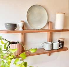 two wooden shelves with coffee cups and plates on them next to a potted plant