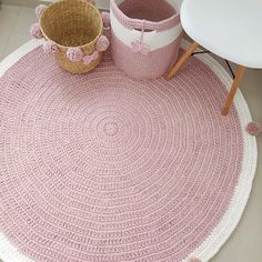 a crocheted pink rug with two baskets on the floor next to it and a white chair