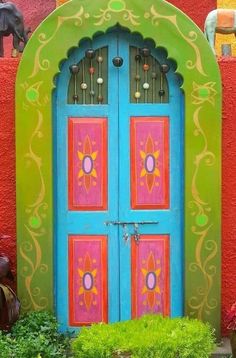 an elaborately painted door is in front of a red wall and green planters