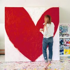 a woman standing in front of a large red heart painted on the side of a wall