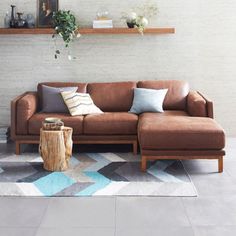 a brown leather couch sitting on top of a white rug next to a wooden shelf