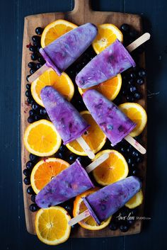 popsicles with blueberries and oranges are on a cutting board in front of a color palette