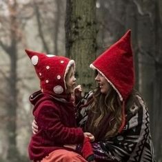 a woman holding a child in the woods wearing red hats with white polka dots on them