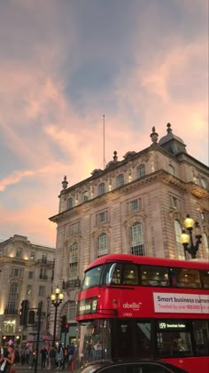 a red double decker bus driving past a tall building