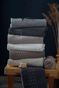 a stack of folded towels sitting on top of a wooden table next to a vase