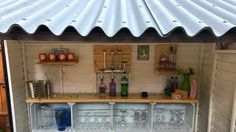 an outdoor bar with lots of bottles and glasses on the top shelf, under a metal roof